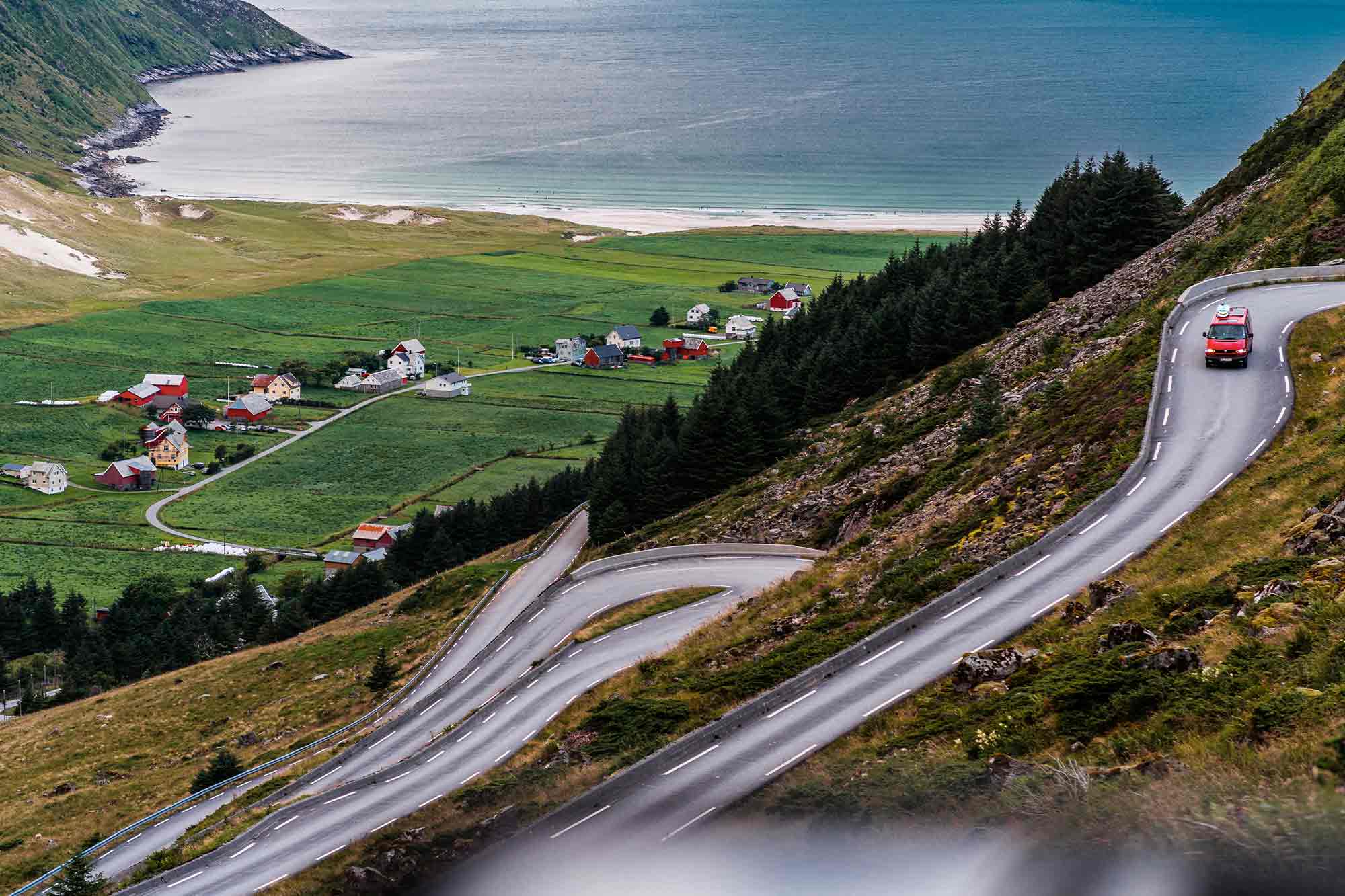Ein roter Campingbus fährt an einem Fjord in Norwegen vorbei